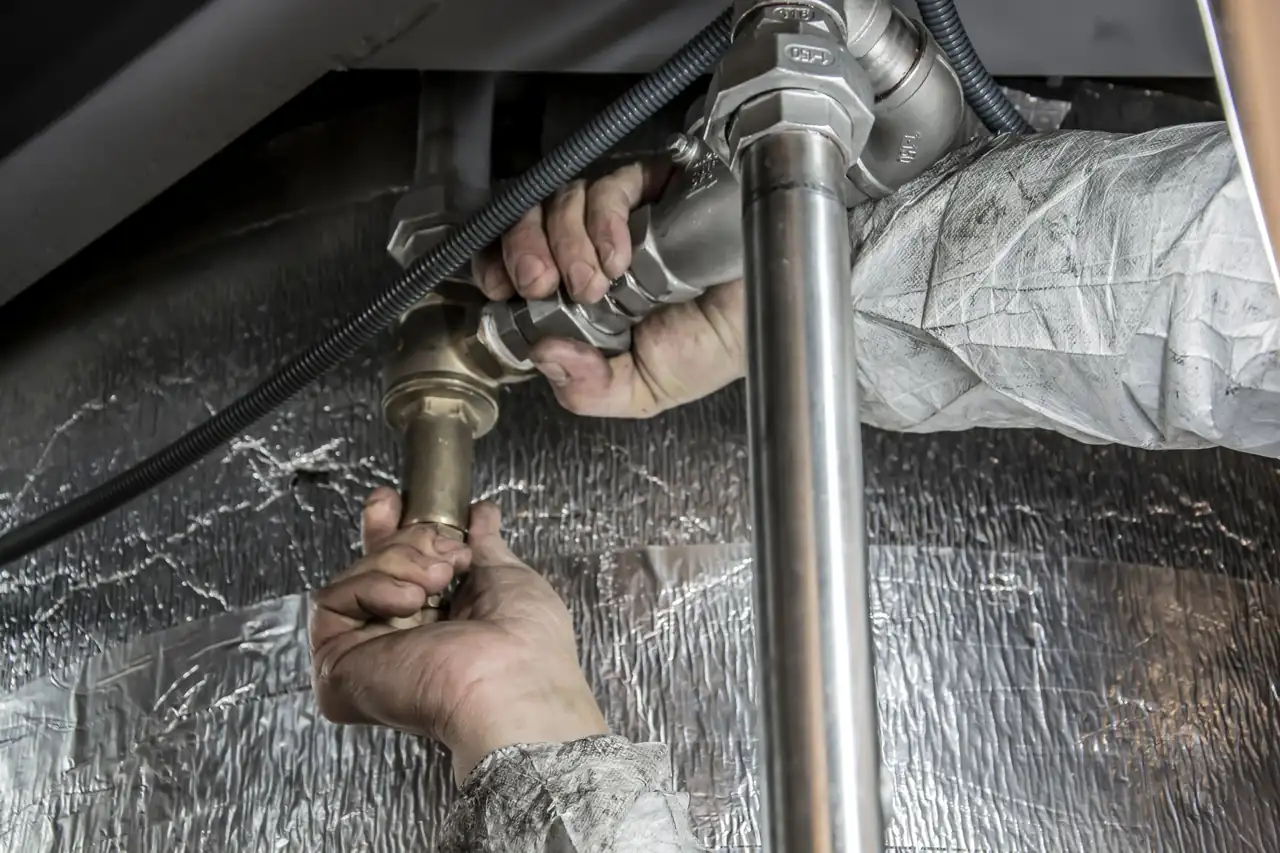 Close-up of hands tightening a fitting on metal water pipes under a sink